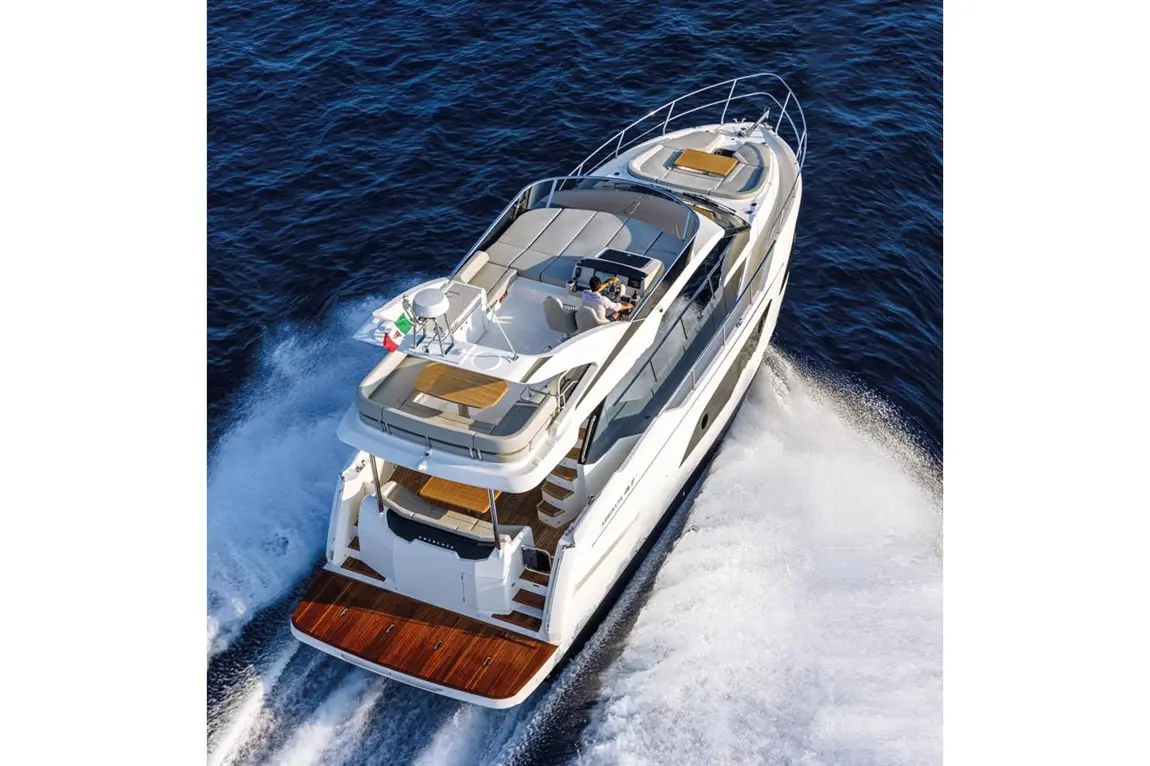 A motor yacht cruising through deep blue waters, featuring a sun deck and a captain at the helm.